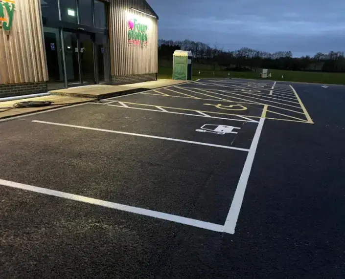 Car park at dusk with a visible line of disabled spaces near a building entrance.