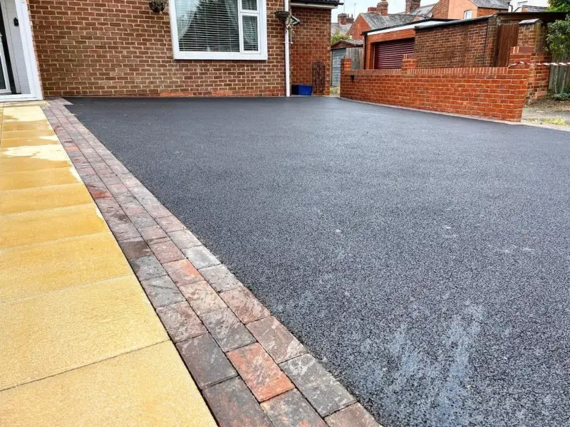 Freshly laid asphalt driveway with a dark, smooth surface, bordered by yellow and red bricks.