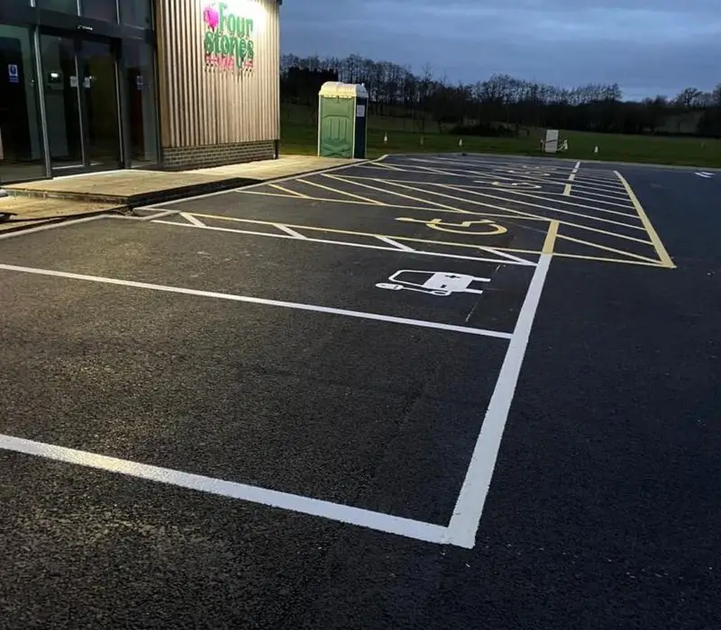 A car park at dusk with marked disabled parking spaces featuring wheelchair symbols.
