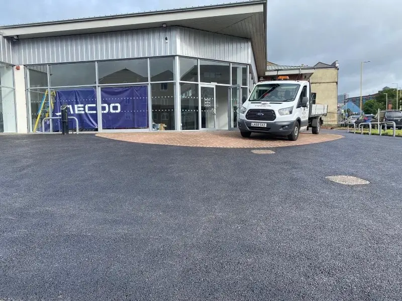 Modern glass-fronted building, next to a large, wet asphalt area, and parked white pickup truck.